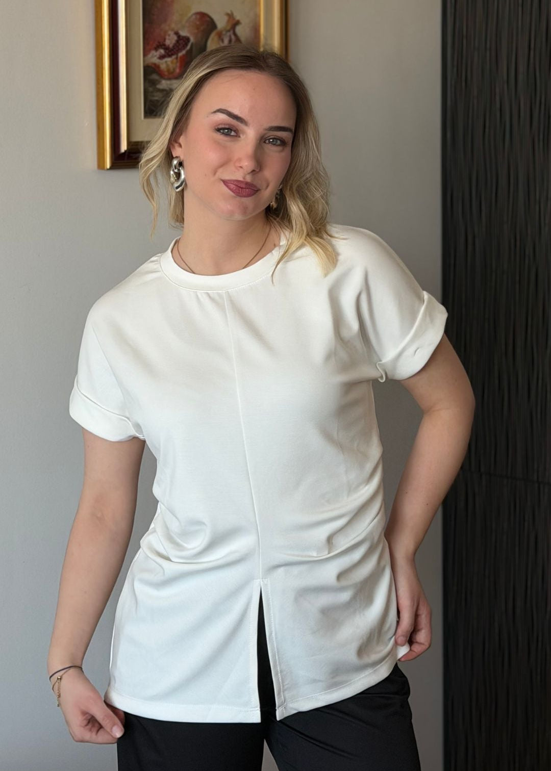 Žena u bijeloj ljetnoj pamučnoj majici Boba s diskretnim prednjim izrezom i bočnim naborima.