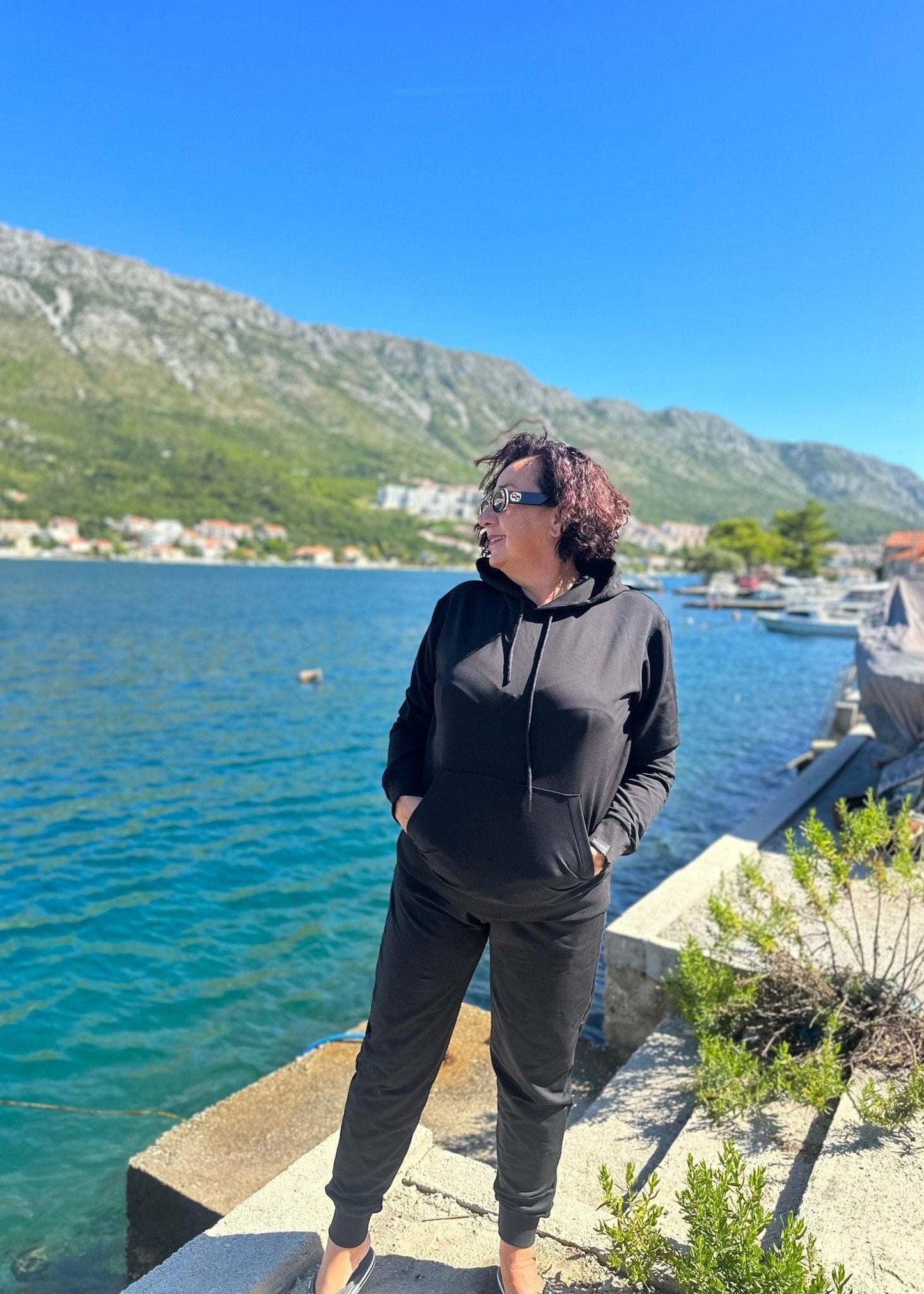 Žena u crnoj trenerci Allure od pamuka i elastina komplet dukserica i donji dio trenerke dubokog struka na obali uz more.