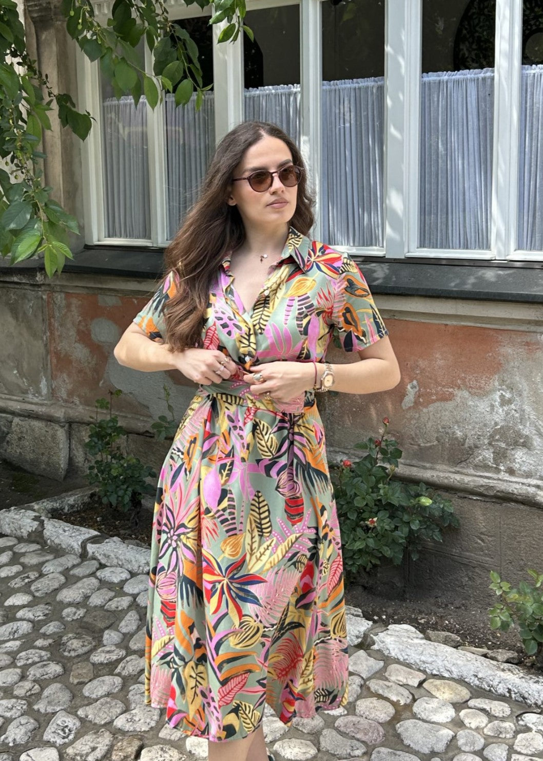 Žena u dezen midi haljini s okruglim vratom na otvorenom, tropski uzorak, naglašen struk i lagana viskoza.