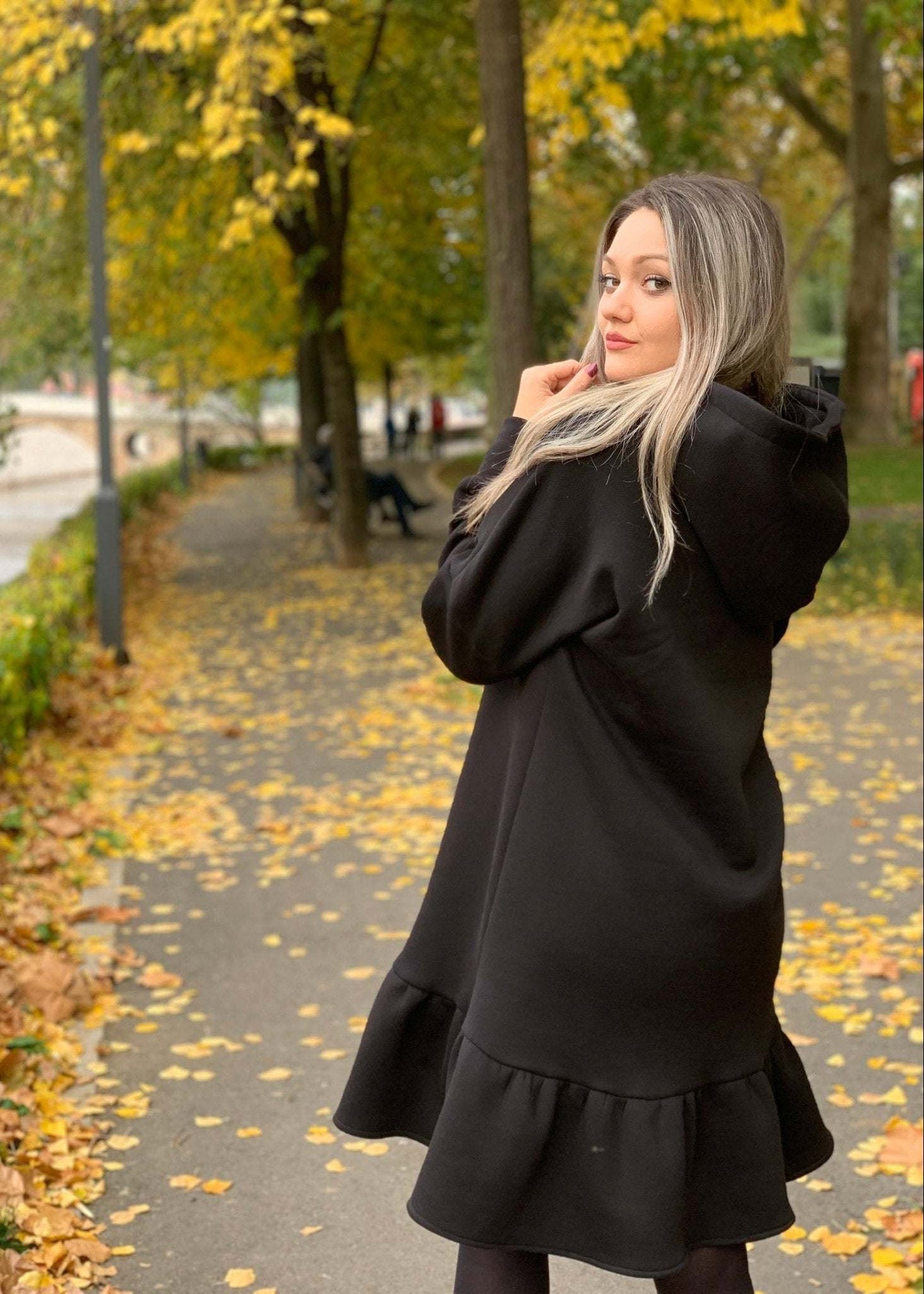 Žena u crnoj midi haljini s rolkom i volanom, urbana vanjska pozadina.