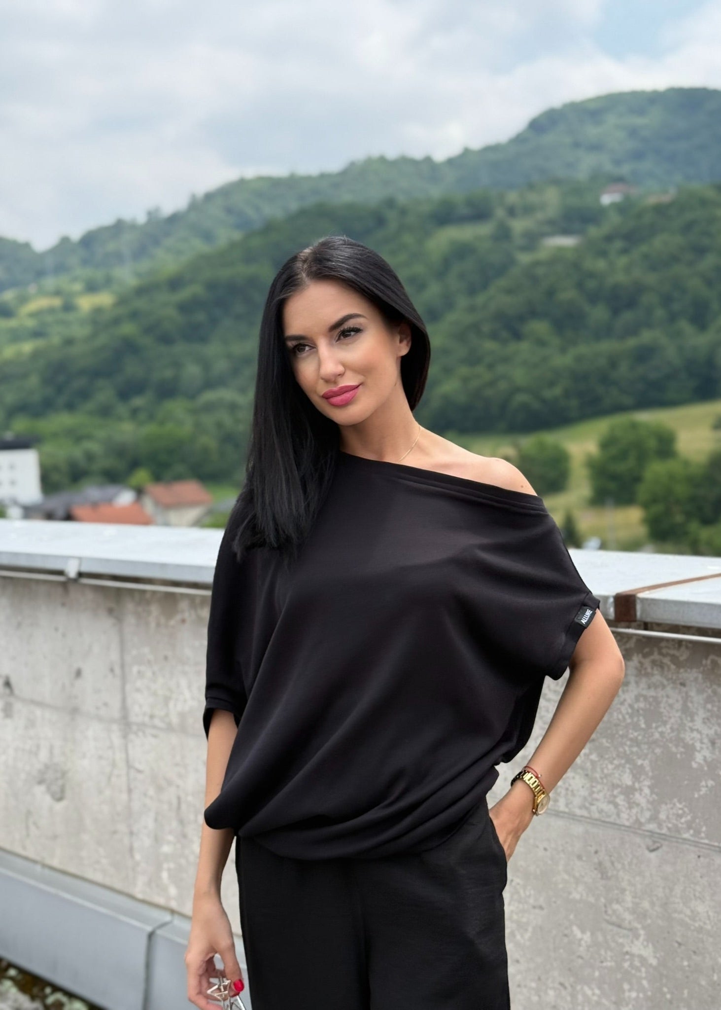 Žena u asimetričnoj crnoj majici Sandra stoji vani na stepenicama.