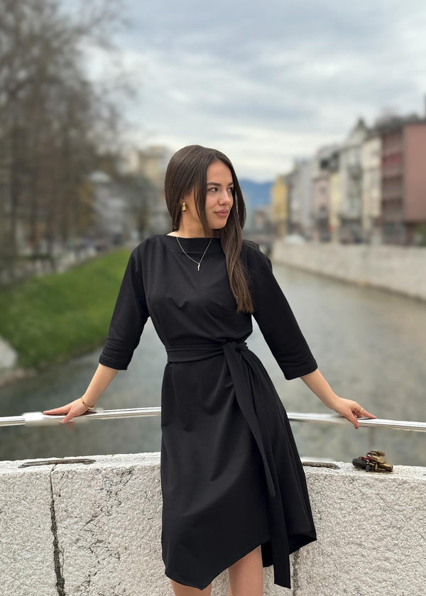 Žena u elegantnoj crnoj midi haljini V s pojasom i 3/4 rukavima.