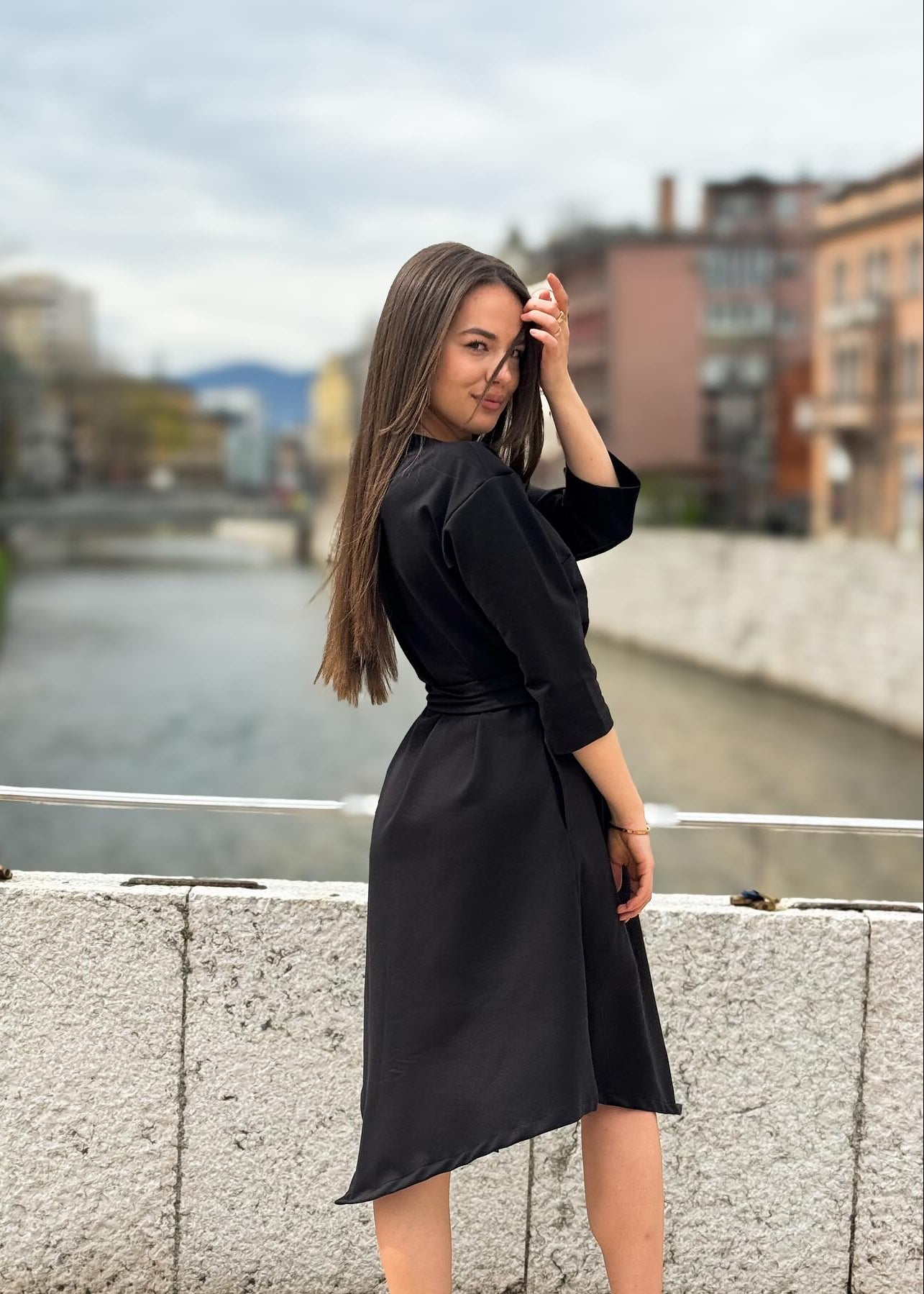 Žena u elegantnoj crnoj midi haljini V s pojasom i 3/4 rukavima.