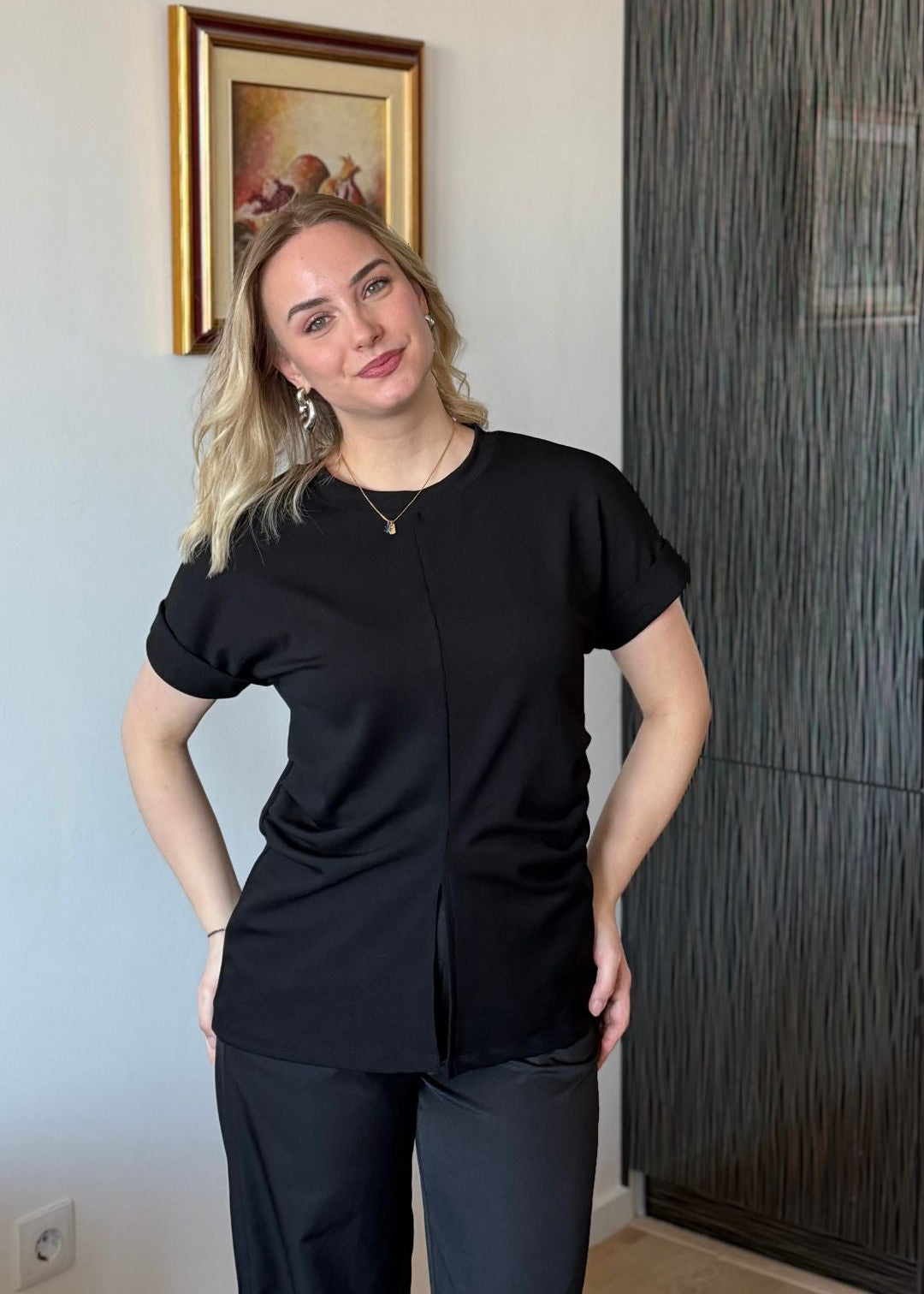 Žena u crnoj ljetnoj pamučnoj majici Boba s diskretnim prednjim izrezom i bočnim naborima.