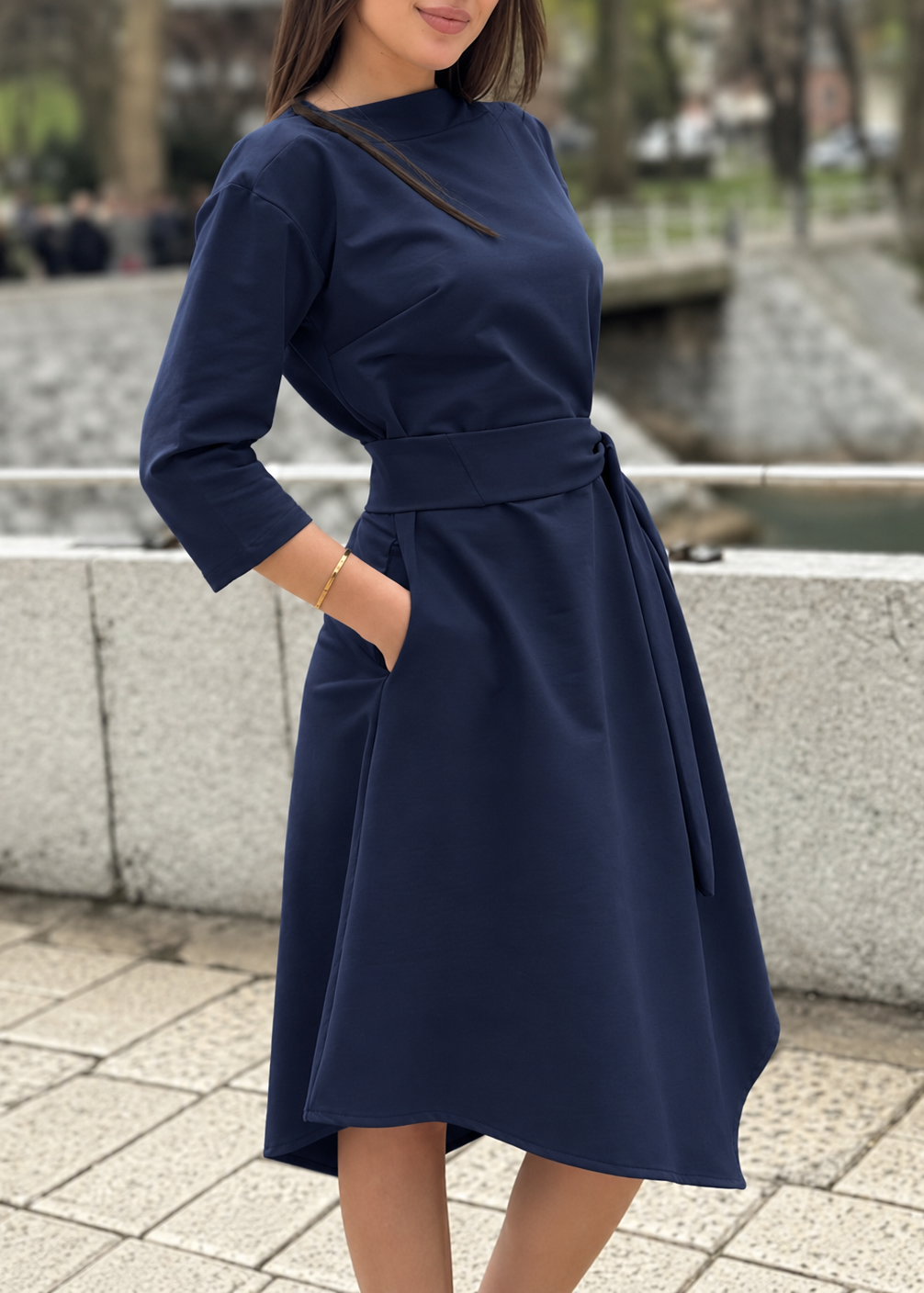Žena u elegantnoj teget midi haljini V s pojasom i 3/4 rukavima.