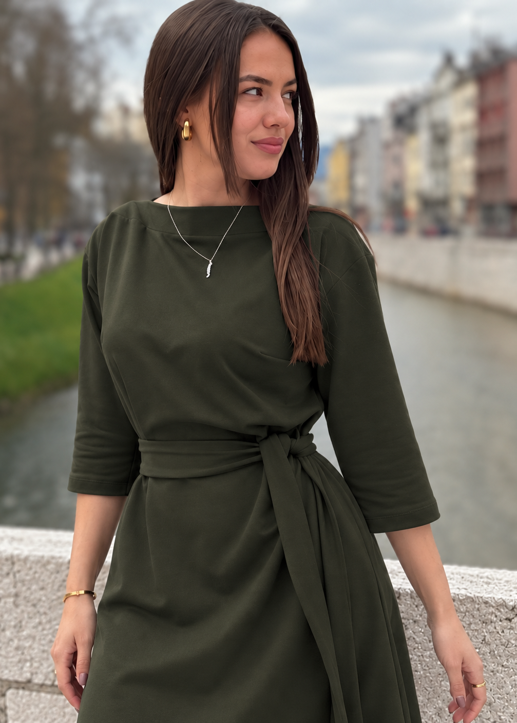 Žena u elegantnoj maslinastozelenoj midi haljini V s pojasom i 3/4 rukavima.