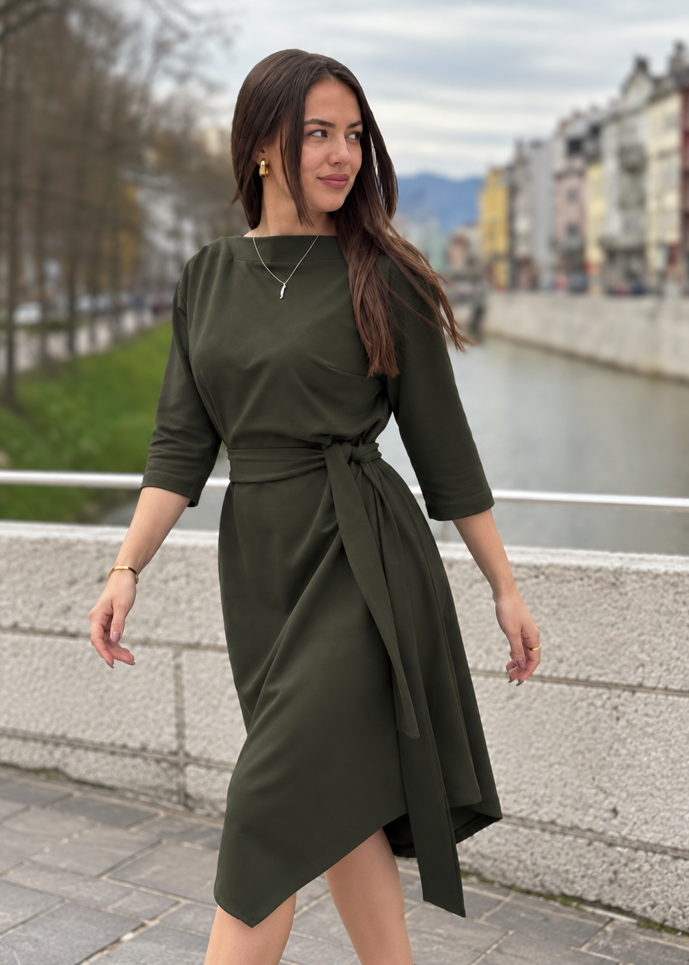 Žena u elegantnoj maslinastozelenoj midi haljini V s pojasom i 3/4 rukavima.