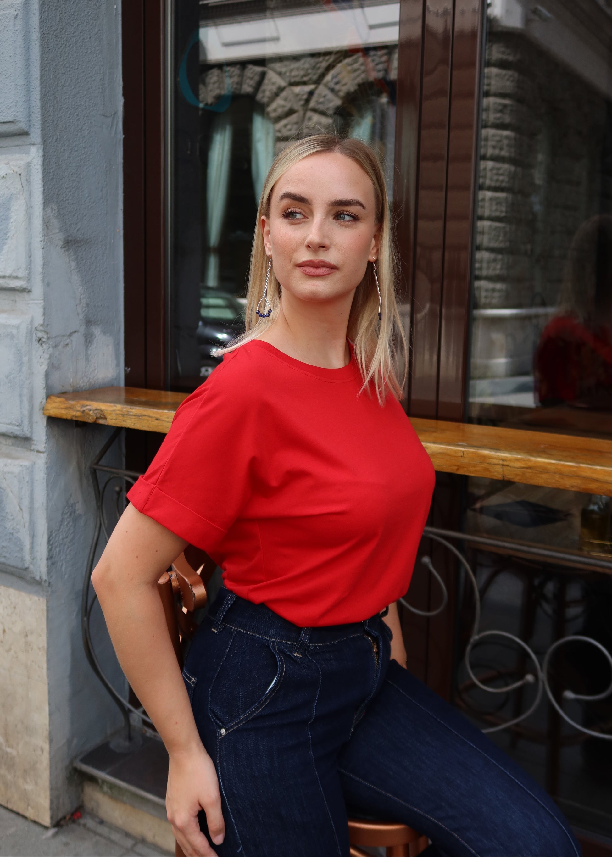 Crvena majica Alisa - model sjedi ispred prozora, bočni pogled