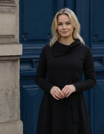 Žena nosi Anita midi crnu  haljinu A kroja s pojasom u struku.