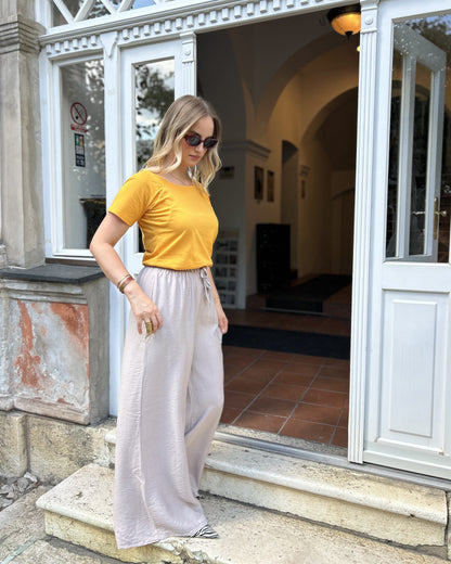Sindy žuta majica — pogled prema dolje, detalj prednjeg dijela i širokih pantalona ispred ulaza
