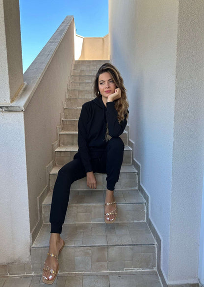 Žena u crnoj trenerci Allure od pamuka i elastina komplet dukserica i donji dio trenerke dubokog struka na stepenicama.
