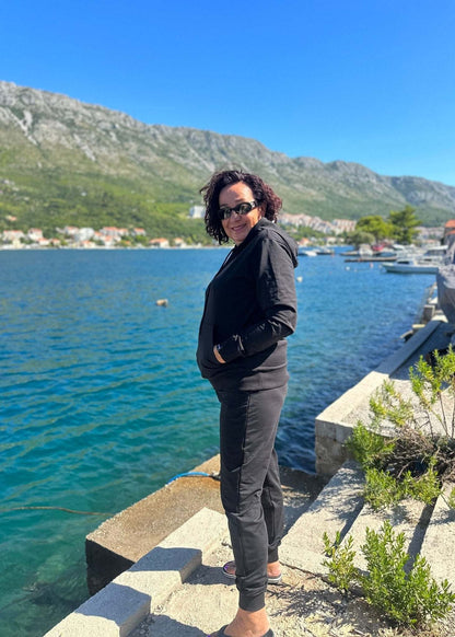 Žena u crnoj trenerci Allure od pamuka i elastina komplet dukserica i donji dio trenerke dubokog struka na obali uz more.