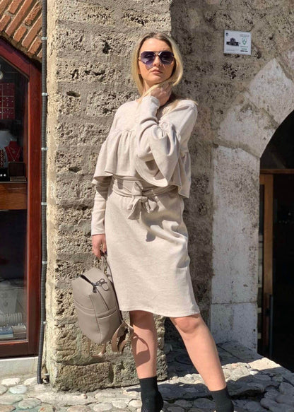 Žena u bež Haljini Roxana ispred kamenog zida sa sunčanim naočarima i torbom