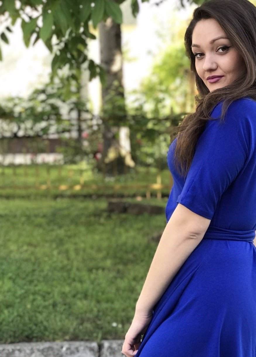 Žena u rozoj Haljini Glok s lepršavom midi suknjom i pojasom, stoji na otvorenom