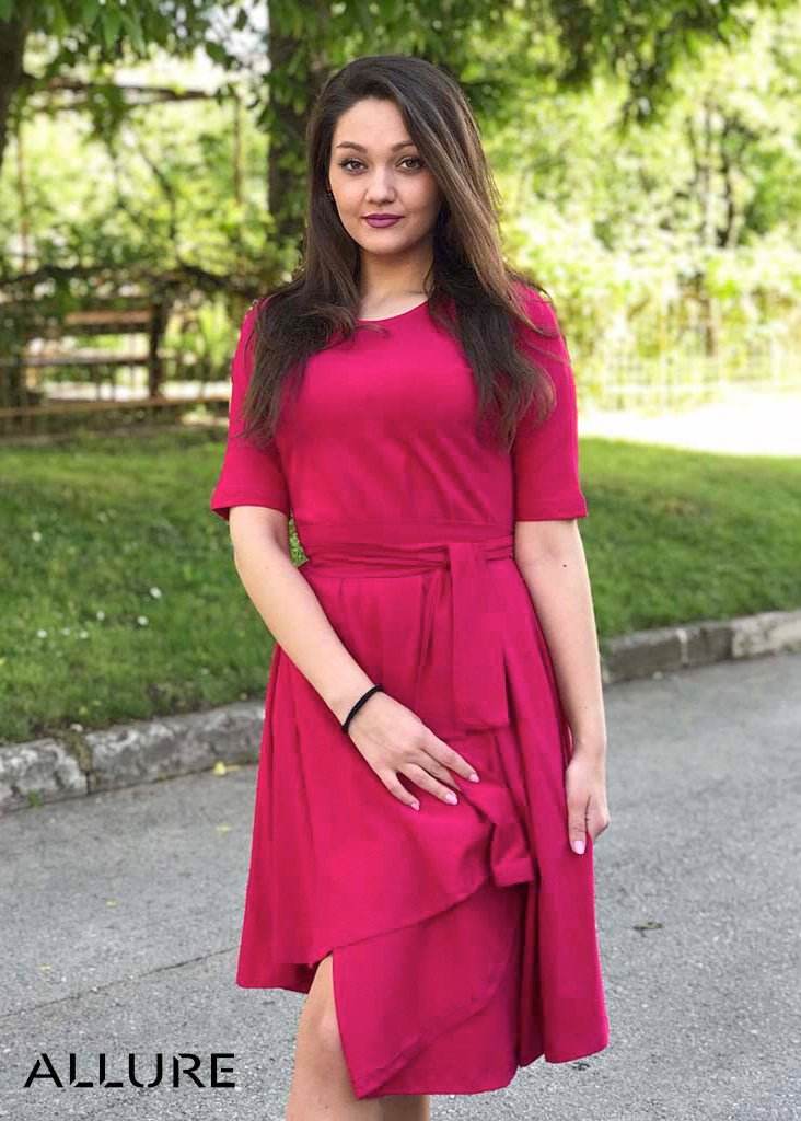Žena u rozoj Haljini Glok s lepršavom midi suknjom i pojasom, stoji na otvorenom