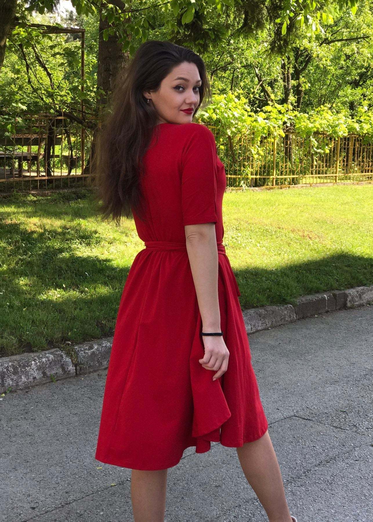 Žena u rozoj Haljini Glok s lepršavom midi suknjom i pojasom, stoji na otvorenom