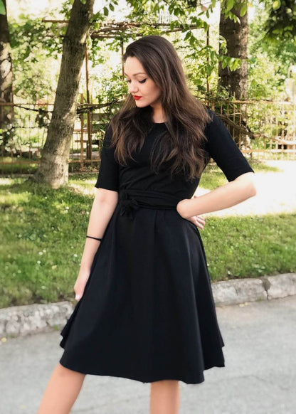 Žena u crnoj Haljini Glok s lepršavom midi suknjom i pojasom, stoji na otvorenom