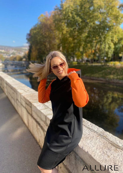 Woman wearing Haljina Jasna black and orange hoodie dress with zipper pocket outdoors in autumn setting