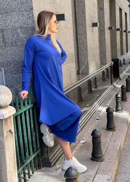 Woman wearing a royal blue maxi dress with high collar and asymmetrical hemline paired with white sneakers outdoors
