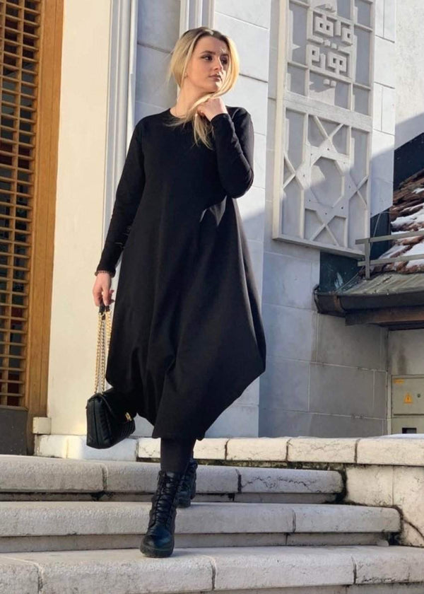 Woman wearing black maxi long sleeved dress with asymmetrical hem and black boots walking down stairs outdoors