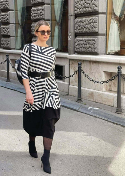 Woman wearing Haljina Erna black and white geometric striped cotton dress with asymmetrical top and black midi skirt walking on city street