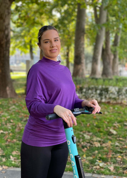 Žena nosi ljubičastu asimetričnu majicu polurolkus dugim rukavima u vanjskom okruženju.