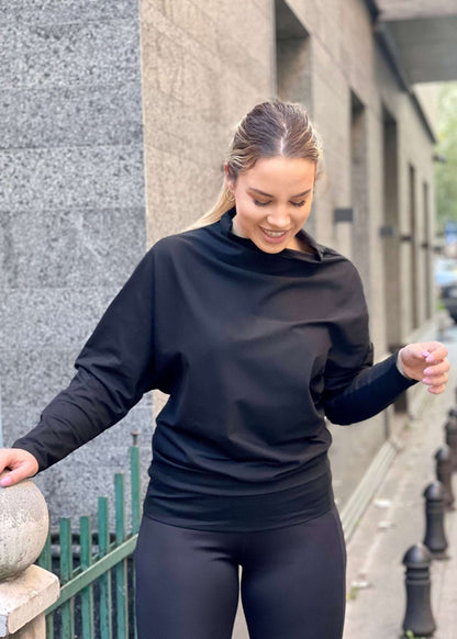 Žena nosi crnu asimetričnu majicu polurolkus dugim rukavima u vanjskom okruženju.