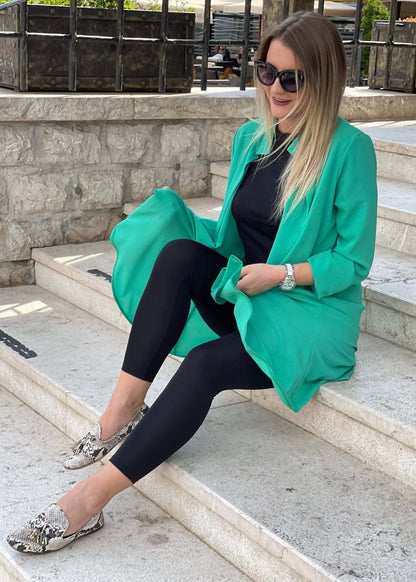 Woman wearing black high-waisted leggings paired with a green blazer and snakeskin flats sitting on outdoor stone steps
